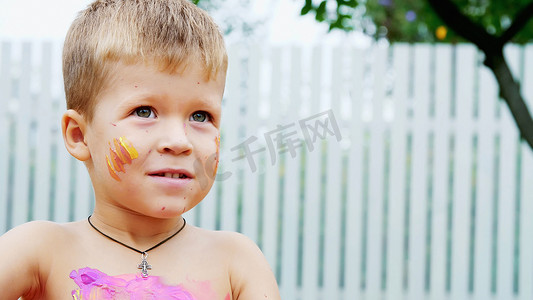 一个小孩子，一个四岁的男孩在夏天玩耍，用手指颜料画画，装饰自己，在花园里，坐在毯子上，在草地上，草坪上。