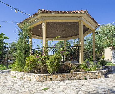 希腊科孚岛西达里教堂花园庭院的黄色凉亭、带鲜花和树木的凉亭