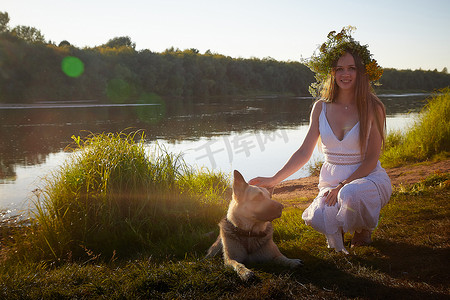 夏天，身穿白色连衣裙、太阳裙和花环的黑发女孩，带着大牧羊犬，在河边或湖边，日落时分，庆祝伊万·库帕拉的异教节日