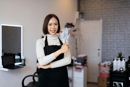 一位年轻的亚洲女美发师拿着合格的理发工具的肖像。