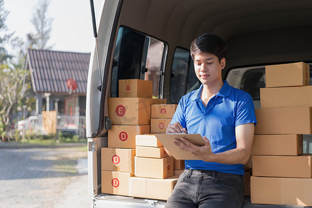 身穿制服的亚洲年轻送货员快递员在汽车附近持有文件剪贴板和箱检查清单包裹邮箱，为客户提供服务，网上购物服务概念