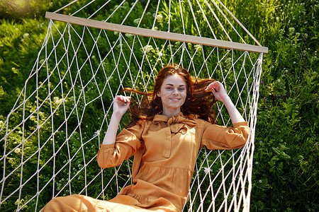 优雅的躺着摄影照片_一位美丽优雅的女士穿着橙色长裙，躺在大自然的网状吊床上，在温暖的夕阳余光的照射下，幸福地微笑着。