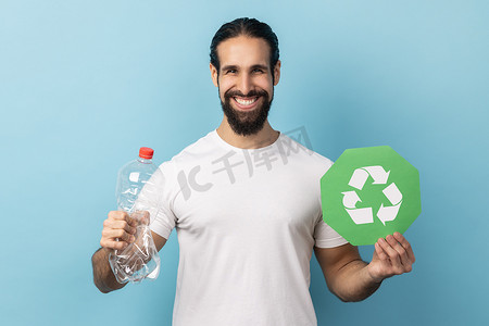 男子拿着空塑料瓶和绿色回收标志，看着相机。