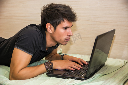 年轻人在卧室里用笔记本电脑做作业