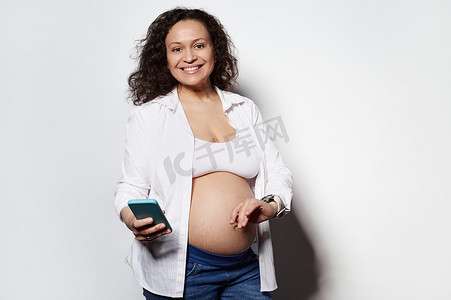 微笑的孕妇在智能手机的移动应用程序上记录宫缩或婴儿动作，对着镜头微笑
