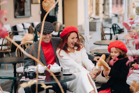 一家时尚的三口之家正坐在咖啡馆外面的桌子旁喝咖啡。
