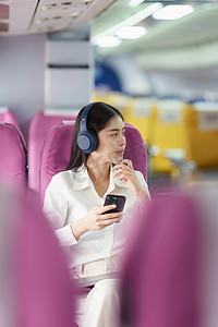美丽的亚洲女商人在飞机飞行时用手机听音乐。