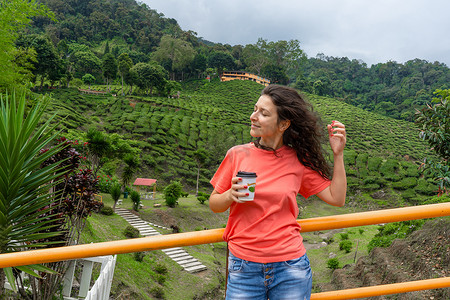 黑发旅游女孩在绿茶谷的背景下享用工艺杯中的茶。