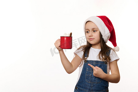 圣诞老人可爱女婴白色的孤立肖像，帽子指着红杯热可可饮料和棉花糖