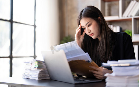压力大的女商人疲惫抑郁年轻职业女商人摸头感觉头痛偏头痛或压力，在笔记本电脑工作和文件后精疲力尽，坐在办公室精疲力竭