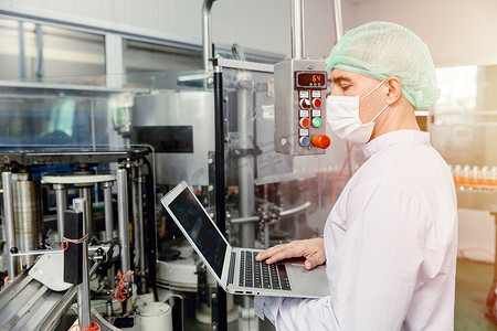 工程师在食品厂机器生产检查员中使用笔记本电脑，穿着卫生服。