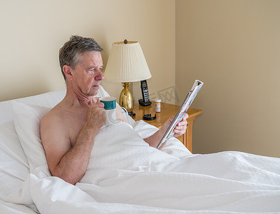 单身白人老人躺在斜床上看杂志