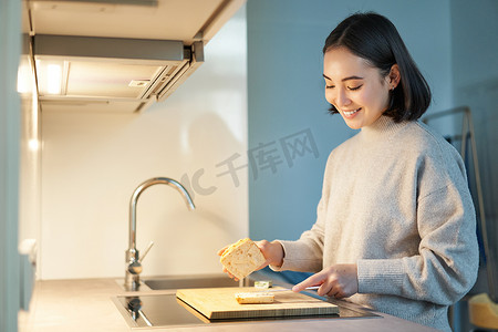 微笑的亚洲年轻女性站在厨房里做三明治、为自己做饭的肖像