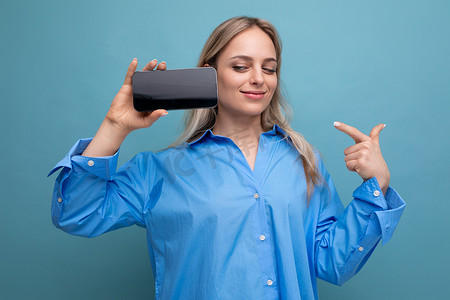 手机app生活摄影照片_成功自信的金发女孩拿着智能手机，上面有蓝色背景应用程序的模板