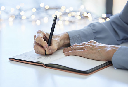 老妇人在规划器中写日历时间表、清单或商业想法的笔记本、笔和手。