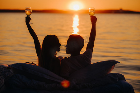 夏日傍晚日落时分，一对幸福夫妇在海边举杯的剪影