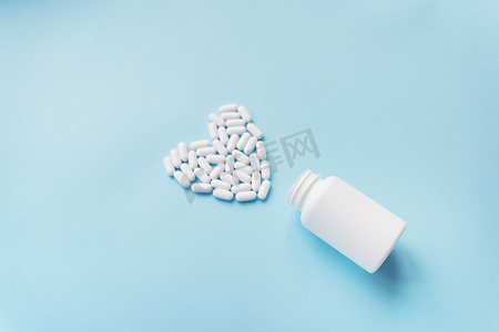 心脏蓝色背景摄影照片_心形的白色药丸从蓝色背景的罐子里出来，健康和心脏问题以及塑料罐。