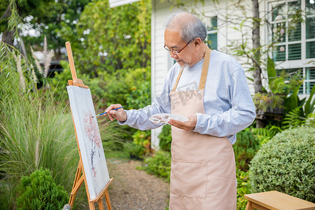 亚洲老人用画笔和油画在画布上绘画