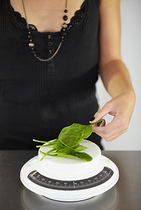 饮食计划摄影照片_厨房里的手、秤和菠菜，用于饮食、食物或饮食失调，并配有叶子用于膳食计划。