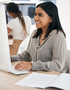 一位印度女性在办公室的桌面上工作，使用电脑、报告和打字。