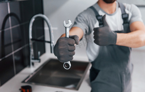身穿灰色制服的年轻专业水管工在厨房里手拿扳手的特写