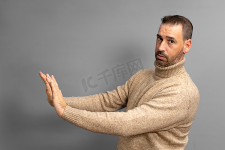 严肃男子的侧视图做出停止手势，显示手掌，冲突禁令警告危险，停止欺凌，穿着米色高领毛衣。