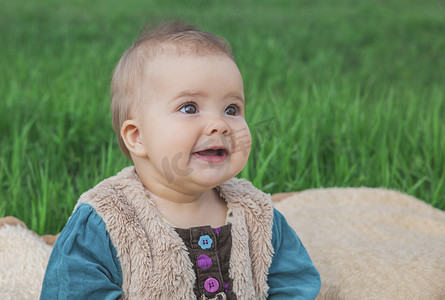 穿着彩色连衣裙的无牙婴儿坐在草坪上的床罩上