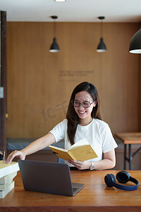 学习少女摄影照片_一名亚洲少女使用电脑和笔记本通过图书馆木桌上的视频会议在线学习的肖像