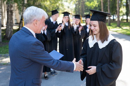老师在室外与学生握手并颁发毕业证书。