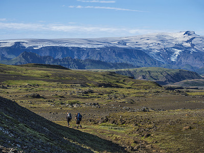 两个年轻的徒步旅行者在洛加维格徒步小径上行走，那里有埃亚菲亚德拉冰盖火山和冰川舌、蓝色的溪流和绿色的山丘。