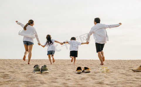 父亲、母亲和孩子脱鞋在沙滩上奔跑