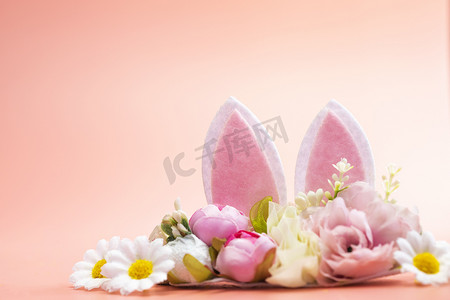 兔子粉色摄影照片_春季假期创意背景，兔子耳朵装饰着淡粉色主题的花朵。