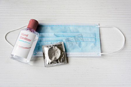 白色背景上的一瓶洗手凝胶、一个避孕套和一个手术口罩。