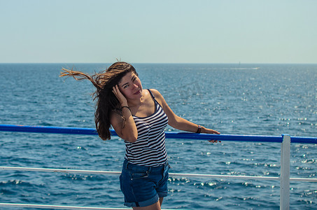 身穿条纹T恤、靠在海边栏杆上的漂亮黑发女孩