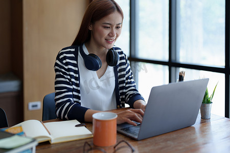 一位年轻、迷人的亚洲少女早上在图书馆上网学习时使用电脑、喝咖啡的肖像