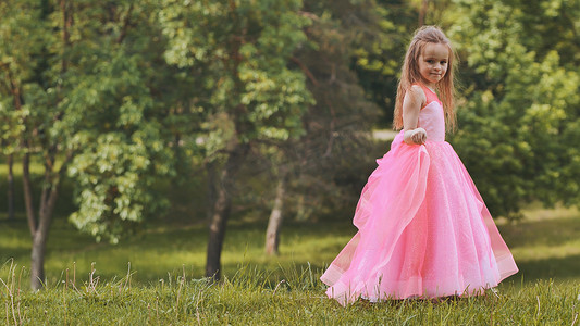 一个穿着粉色公主裙的女孩正在公园里散步。