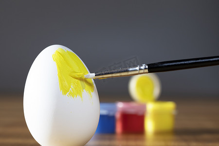 粗刷正在用黄色画一个易碎的复活节彩蛋，为节日快乐复活节概念特写做准备