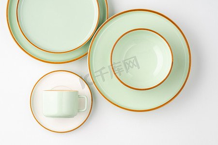 淡绿色卷轴摄影照片_一套带有橙色轮廓的白色和淡绿色陶瓷餐具。