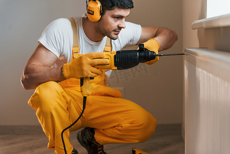 家杂摄影照片_身穿黄色制服的杂工在室内使用锤钻工作。