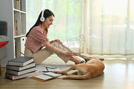美丽的年轻女子戴着耳机和狗玩耍，在家里玩得很开心。