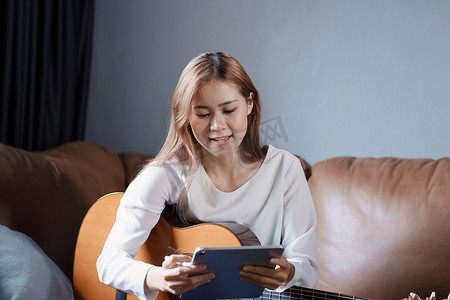 亚洲年轻女性在沙发上弹吉他放松度假压力的肖像