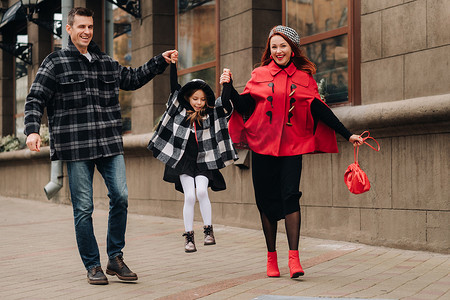 秋天，时尚的三口之家手牵着手在城市里散步