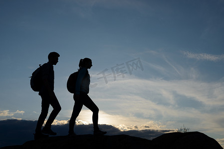 夏日日落时，年轻快乐的旅行者背着背包在岩石小道上徒步旅行。
