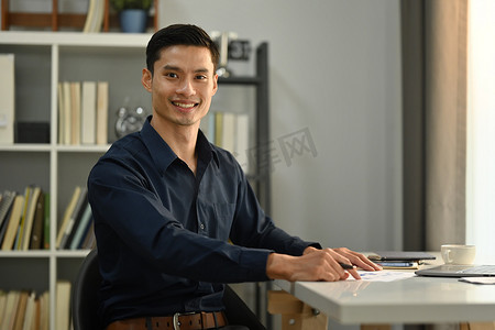 优雅的亚洲商人坐在笔记本电脑前，自信地看着镜头