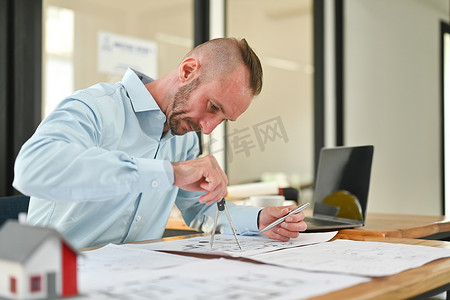 集中精力的白人建筑师正在研究蓝图，在工作站绘制建筑项目草图