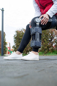 长款包腿护膝摄影照片_腿部手术后佩戴护膝或矫形器的妇女在公园散步