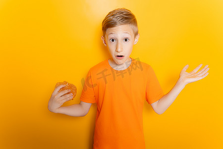 一个穿着橙色T恤的男孩一手拿着汉堡，双臂向两侧张开，表现出困惑的姿态