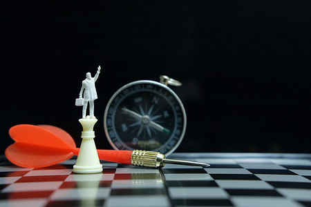 人站在箭头上摄影照片_微型商人站在带有红色箭头的棋盘上的城堡棋子上方