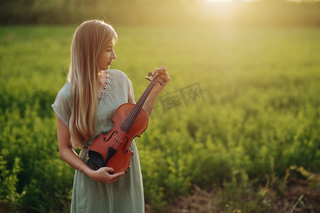 夕阳下，女音乐家小提琴手手里拿着小提琴