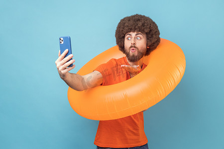 男子手持橙色橡胶圈和手机，进行视频通话，发送飞吻。